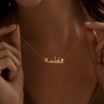 Copper necklace pendant spelling the name Fatima in Arabic calligraphy.