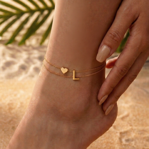Woman wearing a letter L heart anklet with a double-layer chain and heart charm.