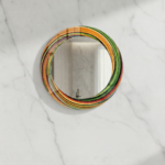 Round tempered glass wall mirror with colorful abstract swirl pattern frame on a marble wall