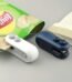 Handheld white mini bag sealer with USB-C port sealing a plastic potato chip bag.