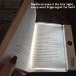 A transparent LED reading light panel placed over a paperback book page in a dark room.